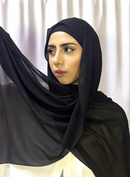 A woman wearing a black chiffon scarf with a non-slip undercap, in a room with curtains.